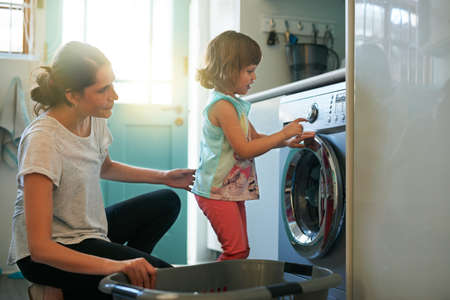 She knows which buttons to press. Shot of a mother and daughter using a washing machine.の写真素材
