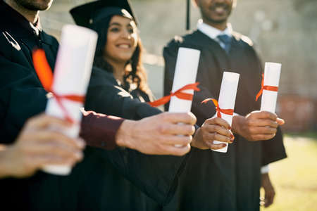 The key to unlocking a rewarding future. Closeup shot of a group of unrecognizable students holding their diplomas on graduation day.の写真素材