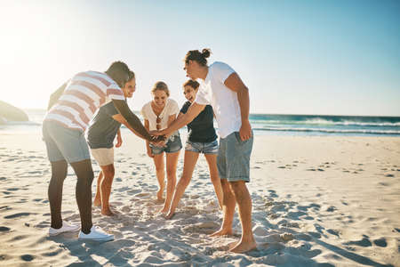 Promise to make this summer the best one yet. Shot of a group of young joining their hands together in solidarity at the beach.の写真素材