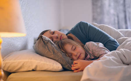 They spend every possible moment together. Shot of a mother and her little girl sleeping in bed together.の写真素材