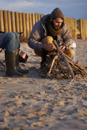 Hell get it started. A young man building a fire on the beach.