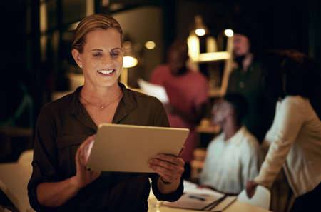 Shot of a businesswoman using a digital tablet in an office at night.の写真素材