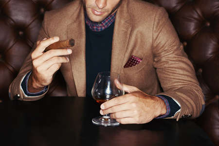Showing off his wealth. A stylish man drinking whiskey and smoking a cigar.