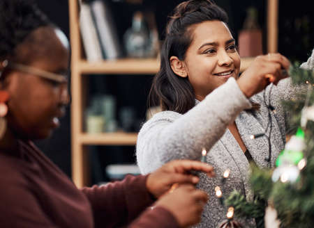 The best Christmases are spent with best friends. Shot of two young women decorating a Christmas tree at home.の写真素材