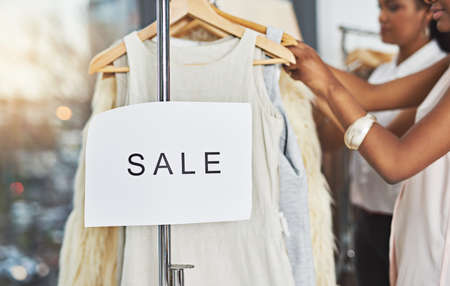 Shopping up a storm. Cropped shot of two women looking at dresses on a rail with a sign that reads...