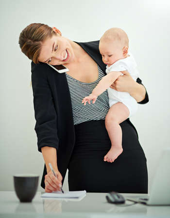 Raising a business and a baby. Shot of a successful young businesswoman carrying her adorable baby boy while talking on the phone.の写真素材