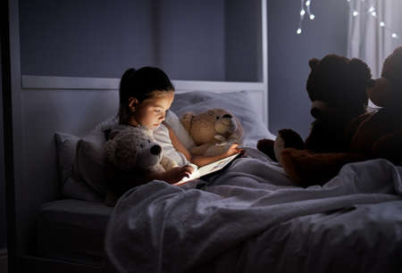 These teddys need their bedtime story. Shot of an adorable little girl using a digital tablet in bed...