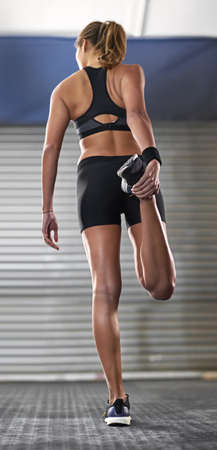 She never forgets to stretch. Rearview shot of a woman stretching her legs before a gym workout.