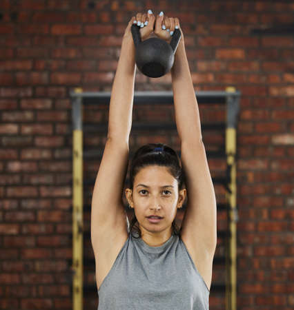 Lifting weights can give you more than just a toned body. Shot of a sporty young woman exercising with a kettlebell in a gym.の写真素材