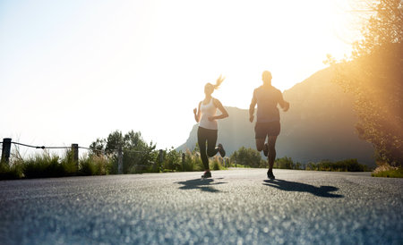 Theres one way to succeed and thats to give everything. Low angle shot of two people running on a tarmac road.の写真素材