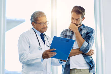 Theres a few things you have to focus on here. Shot of a confident mature male doctor showing test results to a patient inside of a hospital during the day.の写真素材