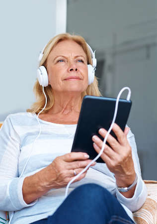 Living the life of a teenager. Shot of a senior woman wearing headphones while holding her digital tablet.の写真素材