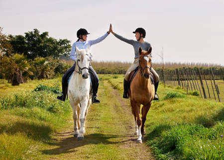 Youre doing great. Full length shot of two young woman high fiving while riding their horses on the ranch.の写真素材