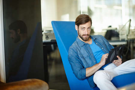Taking care of business online. Portrait of a young businessman using a digital tablet while sitting...