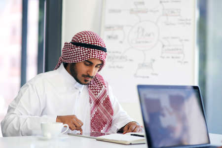 Staying on task with smart technology. Shot of a young muslim businessman using a digital tablet at his work desk.の写真素材