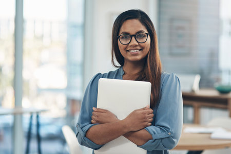 Im excited to explore new opportunities today. Portrait of a young businesswoman holding a laptop while standing in an office.の写真素材