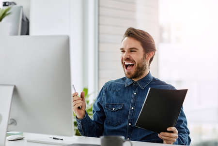 Its a jackpot. Cropped shot of a handsome young businessman cheering while sitting in his office.の写真素材