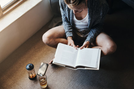 Spending some time alone isnt always a bad idea. High angle shot of a young man reading a book while sitting on the floor at home.の写真素材