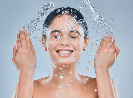 Invest in good skin care. Shot of a young woman washing her face in the shower against a grey background.の写真素材