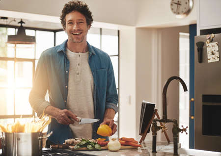 Cooking is a little bit like magic. Portrait of a happy bachelor chopping vegetables in his kitchen.