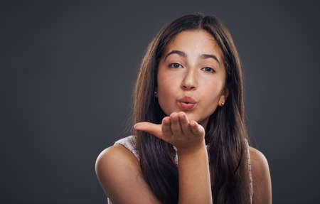 Spread the love. Cropped portrait of an attractive teenage girl standing alone and blowing kisses against a dark studio background.の写真素材
