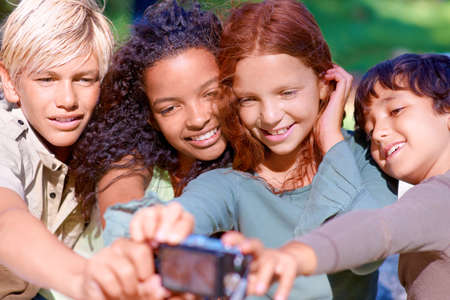 Capturing childhsummer moments. A group of kids looking at a digital camera while sitting outside.
