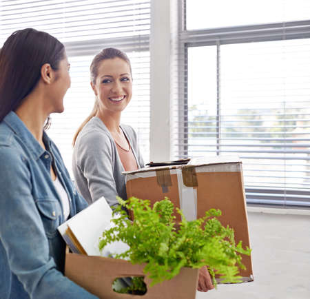 Adding color to the office. Shot of two female entrepreneurs carrying boxes into their new office.
