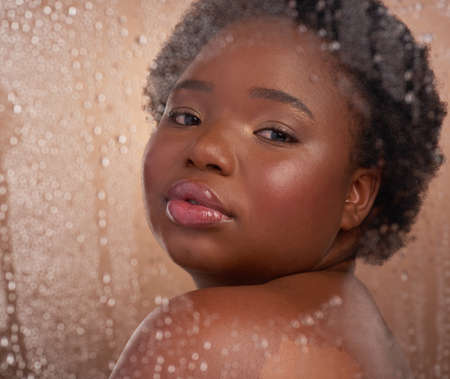 Cleanliness is next to goddessliness. Studio portrait of a beautiful young woman posing against a brown background surrounded by water droplets.の写真素材