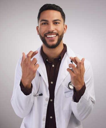 Well...fingers and toes are crossed. Shot of a handsome young doctor standing alone in the studio with his fingers crossed for good luck.の写真素材