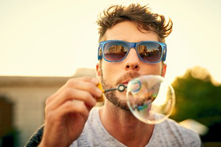 Our inner child never really leaves us. Shot of a young man blowing bubbles outdoors.の写真素材