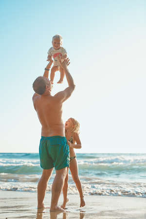 Hes going to be a beach lover. Rearview shot of a man spending time with his son and daughter at the beach.の写真素材