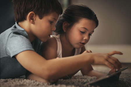 Kid friendly entertainment is just an app away. Shot of an adorable brother and sister using a digital tablet together on the floor at home.の写真素材