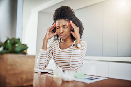 Headache, please go away. Shot of a young woman suffering with a headache while working at home.の写真素材