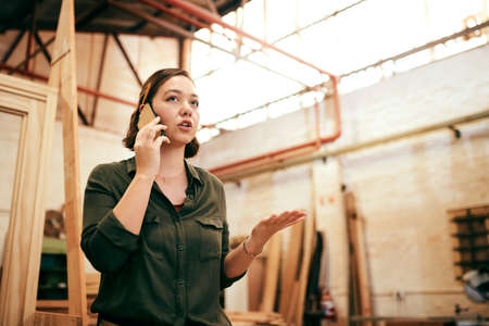 Im always gettin new orders. Shot of a female carpenter talking on her cellphone while standing in her workshop.の写真素材