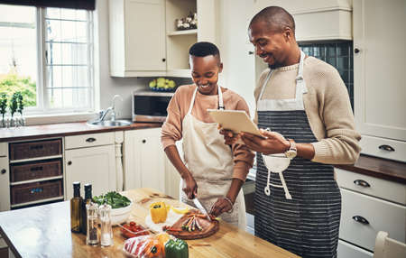 Lets just follow the recipe. Cropped shot of an affectionate young couple using a tablet while preparing dinner in their kitchen.の写真素材