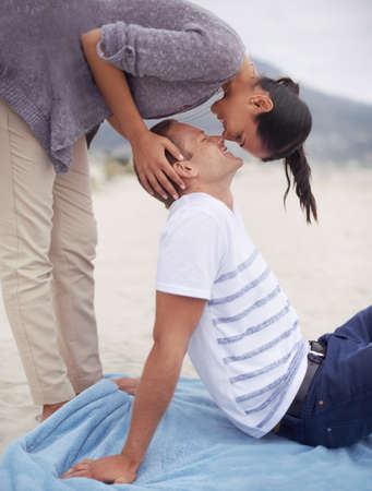 Surprising him with a kiss. Shot of a young woman kissing her boyfriend on the beach.の写真素材