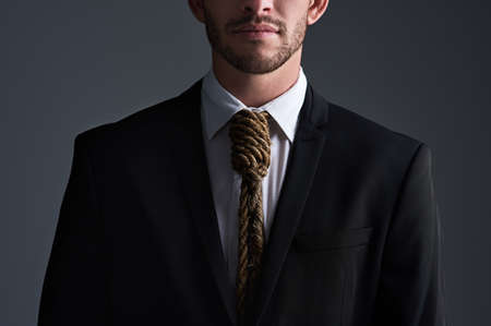Have you become a slave to business. Cropped studio shot of a businessman with a noose tied around his neck for a tie against a gray background.の写真素材