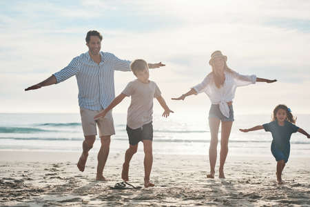 Its a race. Full length shot of a happy young couple enjoying a playful day out with their two children on the beach.の写真素材