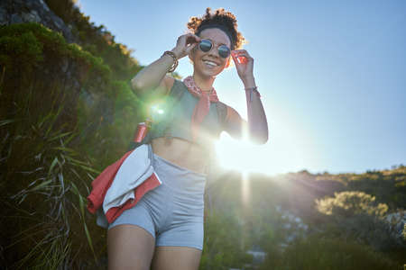 It crazy cool up here. Shot of a young woman wearing her sunglasses while out on a hike.の写真素材