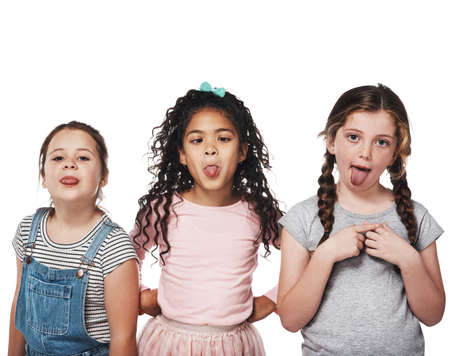 The best part of friendship is having lots of fun. Studio portrait of a group of three girls sticking out their tongues against a white background.の写真素材