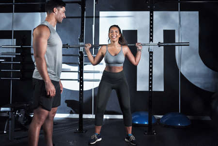 Fine tune your technique, fine tune your body. Shot of a young woman lifting a steel pole during her workout at a gym.の写真素材