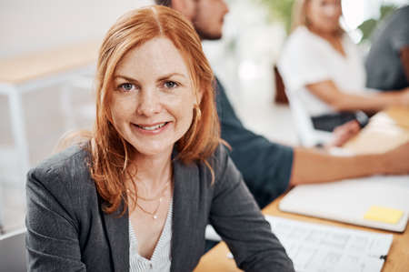 I know Ill achieve success in this company. Portrait of a mature businesswoman sitting in an office with her colleagues in the background.の写真素材