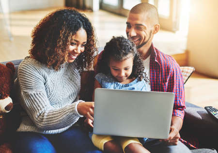Connecting as a family isnt too hard with todays technology. Shot of an adorable little girl and her parents using a laptop together on the sofa at home.の写真素材