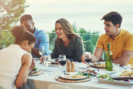 We always have the best times together. Shot of a group of friends enjoying a meal and drinks together around a table at a gathering outdoors.の写真素材