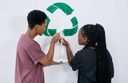 Dont throw your tomorrow awayrecycle. Shot of a young couple painting a recycle symbol on a wall.の写真素材