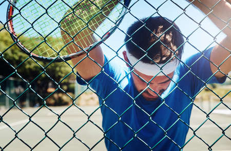 I need to catch my breath. Cropped shot of a handsome young sportsman taking a moment to breathe during tennis practise.の写真素材