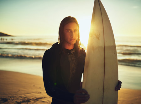 Being a surfer is simply in my blood. Portrait of a young man standing with a surfboard at the...