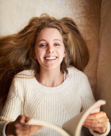 Reading is my favourite hobby. Portrait of an attractive young woman reading a book while lying on...