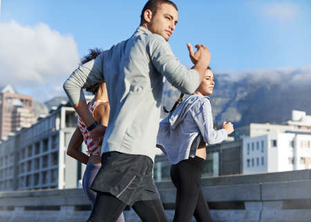 We push each other further. Shot of a group of friends jogging together through the city.の写真素材