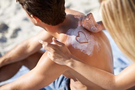 She shows her love where ever she can. A young woman making a heart shape with sunscreen on her boyfriends back.の写真素材